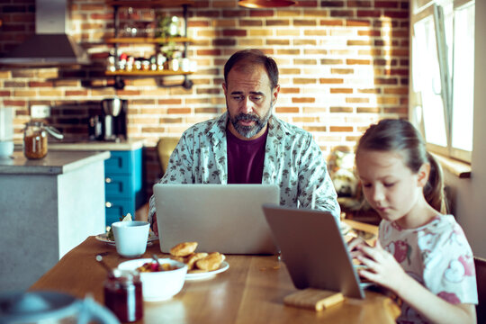 Man working on laptop while girl uses tablet at kitchen table