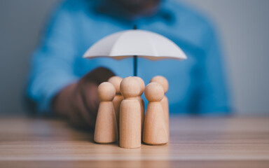 Obraz premium Insurance protection, security, safety, healthcare concept, hand holding an umbrella over group of wooden people figures.