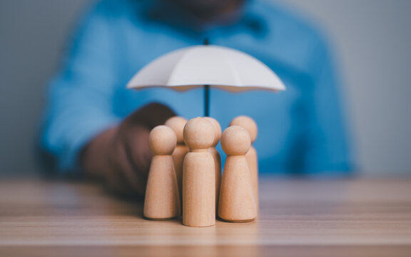 Insurance protection, security, safety, healthcare concept, hand holding an umbrella over group of wooden people figures.