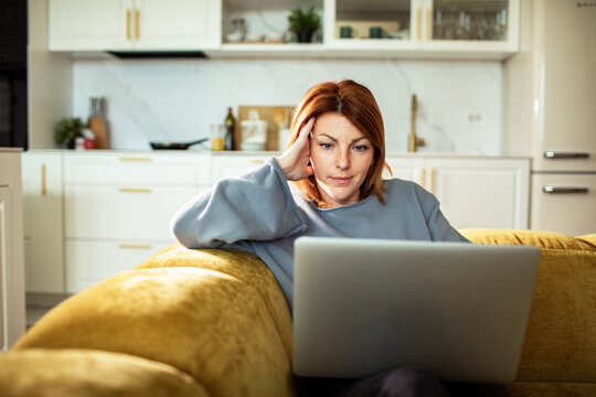 Focused woman using laptop on couch at home