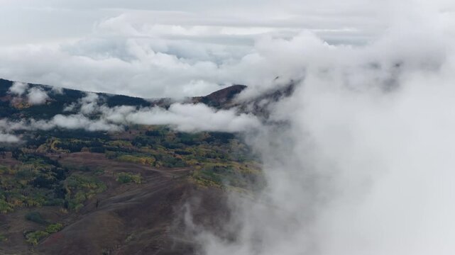 Aerial of mountainous landscape with rolling hills and patches of autumn foliage under heavy low clouds near Crested Butte South Colorado