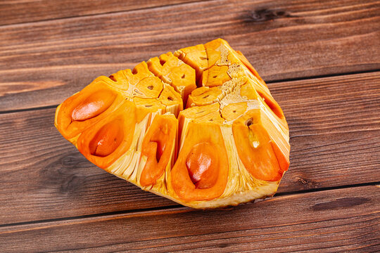 Slice of jackfruit with vibrant orange flesh and visible seeds resting on rustic wooden surface