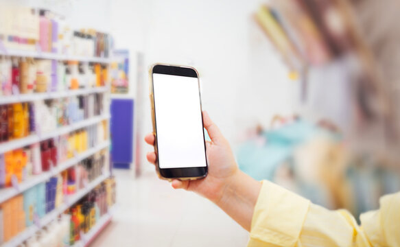 Hand holding smartphone mock up with blank screen in a retail store aisle filled with colorful product packaging and blurred background elements
