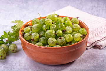 Fresh green gooseberries in terracotta bowl with leaves on textured surface beside folded cloth © Andrei Starostin