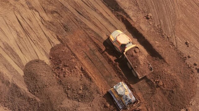 Aerial view of heavy machinery including a dump truck and bulldozer working on earthworks at the Black Cat Roundabout construction site in Chawston, England, United Kingdom.
