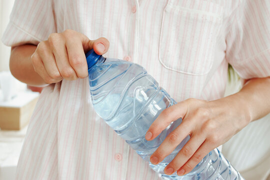 Close-up of hands removing the blue cap from a large transparent plastic drinking water bottle.