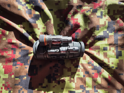 BALTIC STATES - September 28, 2026: A MUM-14 night vision monocular by ACT in Black placed on digital camouflage fabric, displaying compact tactical optoelectronics.