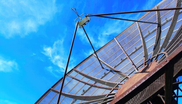 A close-up view of a large parabolic antenna against a clear blue sky.