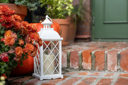 Autumn decoration with white lantern, pumpkin and orange flowers on brick steps near house entrance in daylight with copy space