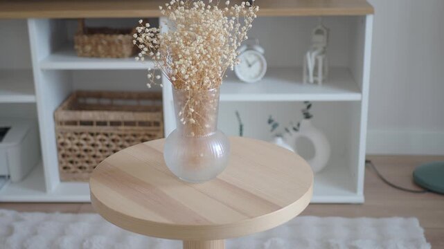 Close up slow motion of dried flowers in a vase on a small wooden table in a bright room.