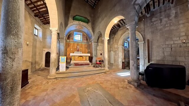 Interior of the ancient Romanesque Church of Santa Maria dei Lumi in Bassano in Teverina, Italy, showing the stone columns, round arches, and rustic wooden truss ceiling of the nave