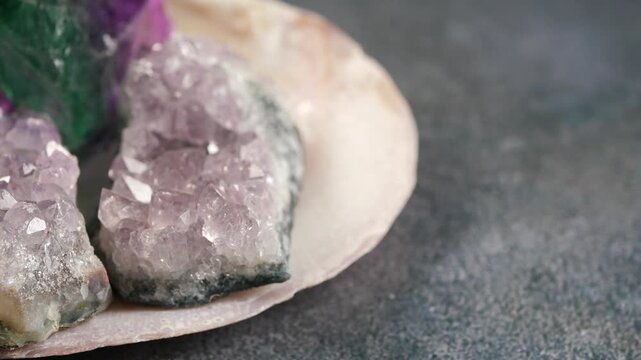 Close up of amethyst and fluorite crystals displayed in a shell on a dark textured surface, slow motion.