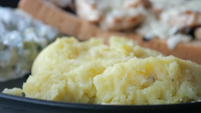 Close up cinematic footage of creamy mashed potatoes on a black plate with blurred background, dynamic view of a delicious meal.