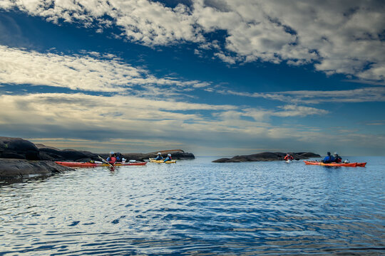 Expedition kayakers paddling among dark granite islands under a dramatic cumulus sky, copy space above and below, Georgian Bay, Ontario