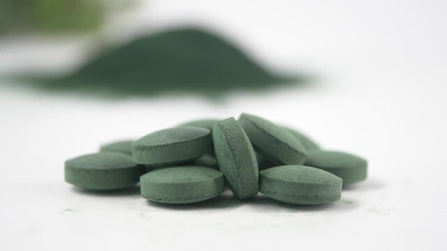 Macro view of green spirulina algae tablets and powder on white background representing natural superfood nutrition.