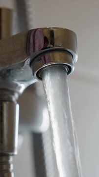 Close up view of chrome faucet with steady stream of clear running water. Soft lighting highlights reflective surface and texture detail background remains out of focus