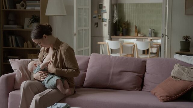 Young adult Caucasian mother breastfeeding infant child at home. Footage highlights postpartum wellness, pediatric care, and lactation support for parenting campaigns