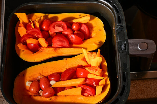 butternut squash halves filled with tomatoes and grapes cooking in an air fryer basket