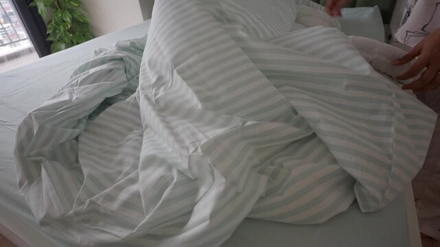 Woman laying out striped duvet cover on freshly made bed in bright modern bedroom morning routine.