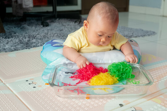 Asian Infant Enjoying Tummy Time Sensory Game with Colorful Spaghetti Noodles in Baking Dish