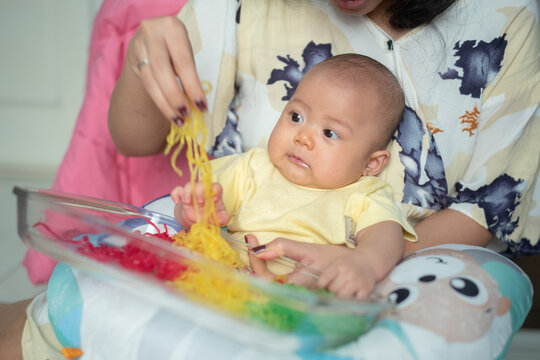 Mother Guiding Asian Baby During Sensory Play Activity with Colorful Spaghetti Noodles