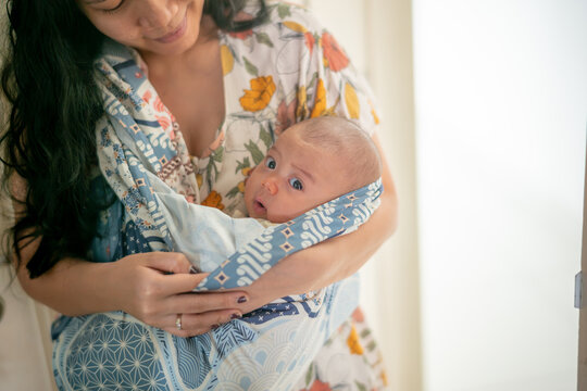 Asian Mother Carrying Baby in Traditional Batik Sling Wrap or Baby Carrier Indoors