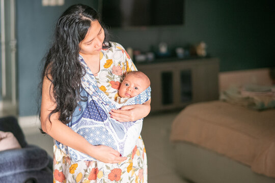 Asian Mother Standing in Living Room Holding Infant in Traditional Patterned Sling Wrap