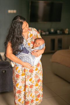 Asian Mother Carrying Baby in Traditional Patterned Sling Wrap Indoors at Home