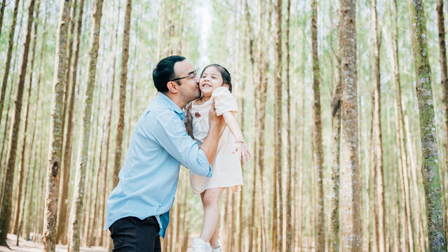 Playful family moment, father holds happy little girl up high, throwing up in sky at park forest. cheerful child enjoy moment playing freedom and joy