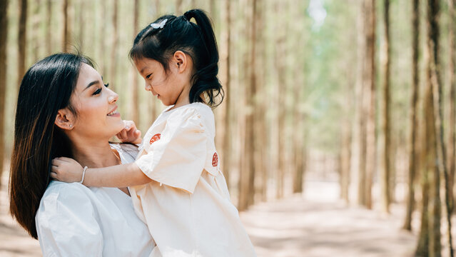 Asian mother carrying a daughter in arms in a peaceful forest setting, Happy smile mother and little child playing together outdoor