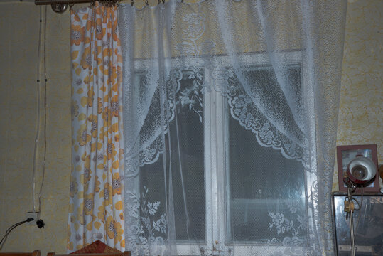 Cozy rustic room interior with a wooden ceiling, lace curtains, floral drapes, vintage furniture, and a window.