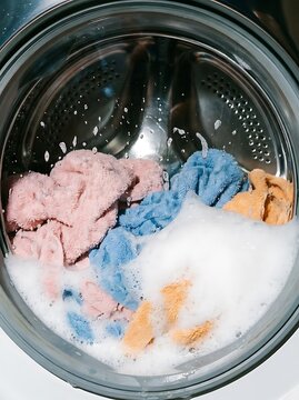 Washing machine drum filled with colorful pink, blue, and yellow towels and soapy water suds during a cycle