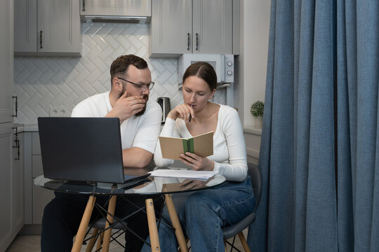 Couple sitting at a table in their kitchen, analyzing personal financial documents and using a laptop, representing remote work, budgeting, and shared household responsibilities