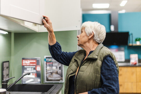 Older Woman Opening Kitchen Cabinet in Home Improvement Store