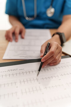 Medical professional reviewing an ECG heart rhythm tracing with a pen, representing cardiac monitoring, cardiology analysis, diagnosis, and healthcare.