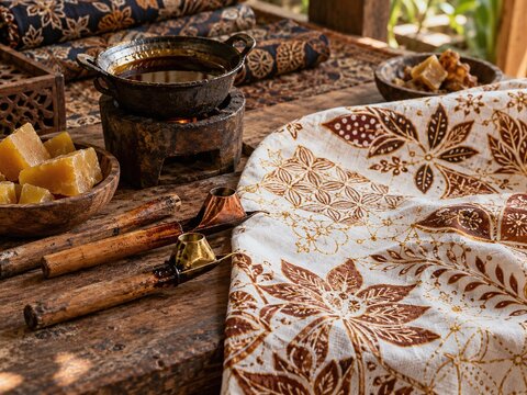 Traditional Indonesian batik workspace with canting tools, melted wax and handmade patterned fabric on a rustic artisan table, representing cultural craftsmanship and textile heritage.