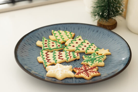 Blue ceramic plate is holding decorated christmas sugar cookies on white countertop near window