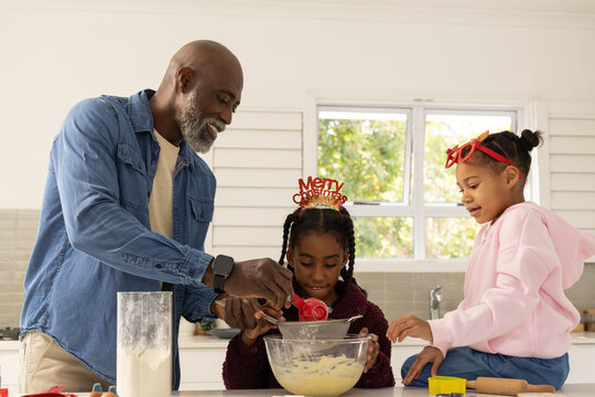 Mature male guiding two youth females sifting flour and mixing in glass bowl in kitchen christmas