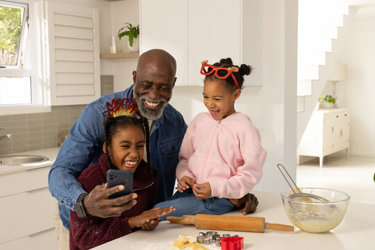 African family baking christmas cookies in bright kitchen using smartphone and rolling pin