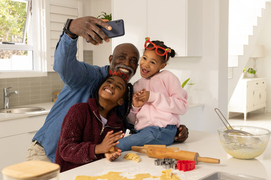 African family senior man and kids taking Christmas cookie selfie kitchen counter with rolling pin