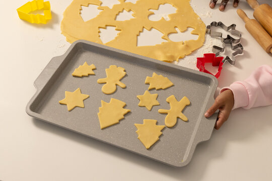 Caregiver and youth holding speckled baking tray with Christmas cookie cutouts on home countertop