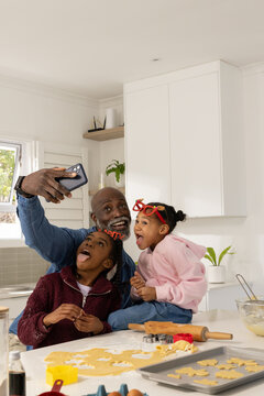 African family with two youth taking christmas selfie in kitchen with cookie dough and smartphone