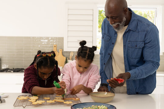 African family Senior guiding two female youths decorating christmas cookies with icing in kitchen