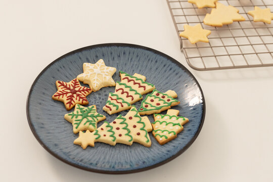 Blue ceramic plate is holding iced christmas tree and star cookies on white tabletop, rack beside
