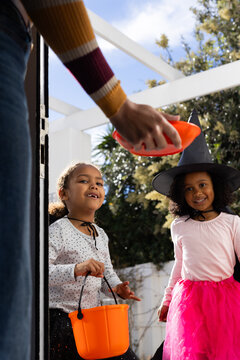 African American girls waiting on porch with orange bucket for halloween, resident handing candy
