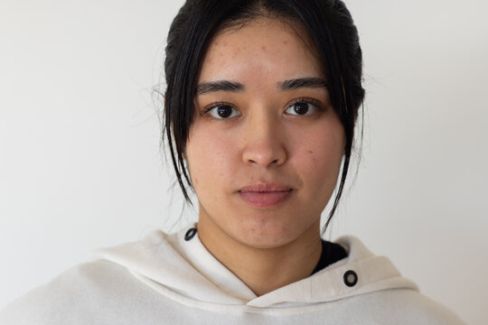 Woman wearing light hoodie with black grommets and dark top looking at camera in studio
