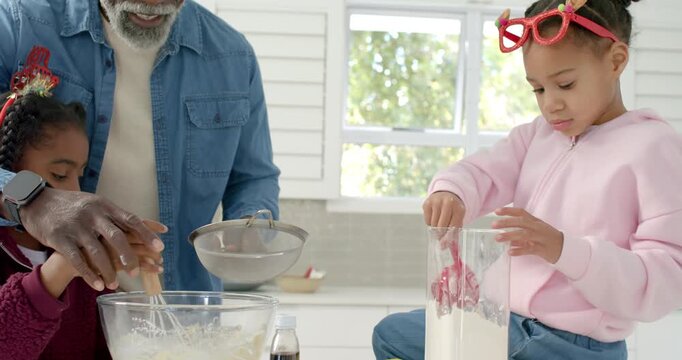 African American family whisking and sifting flour using sifter in kitchen for christmas baking