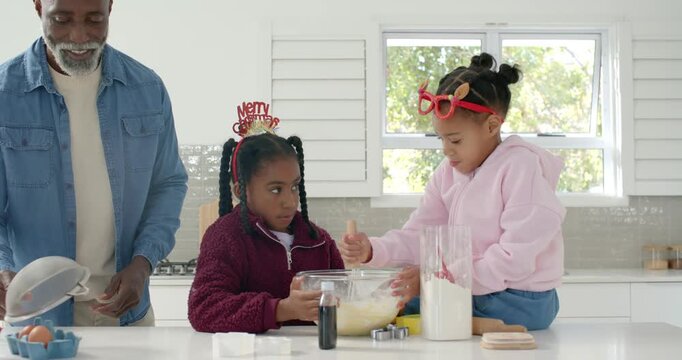 African American family prepping, girls whisking batter in bowl at kitchen counter for christmas