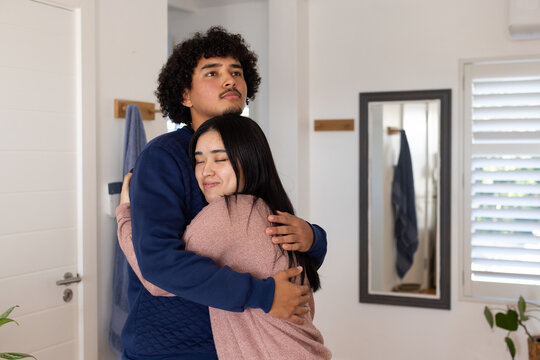 African couple embracing, man in navy sweatshirt and woman in pink cardigan in entryway mirror