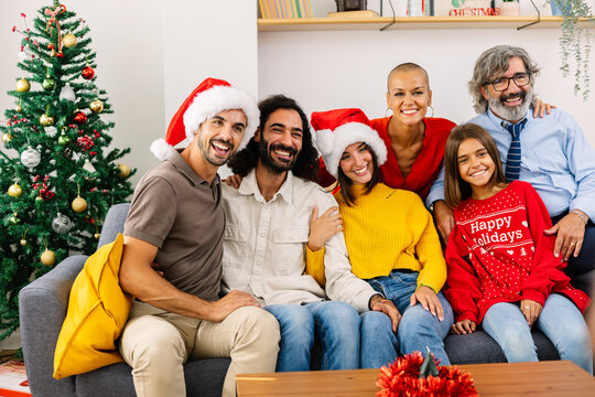 Portrait of happy multigenerational family on sofa at Christmas. Smiling caucasian people of different ages looking at camera in decorated living room. Family and holiday concept.